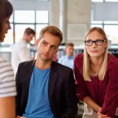 Ein Mann und eine Frau hören aufmerksam zu, während eine Kollegin spricht. Ein Beispiel für **talent mobility** in einem modernen Büro.