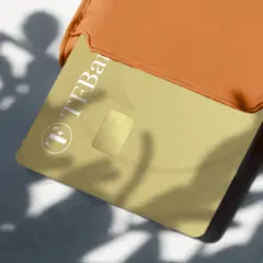 Goldene TF Bank Karte in einem orangen Etui, Schatten von Blättern. Gute TF Bank Erfahrungen sind hier zu sehen.