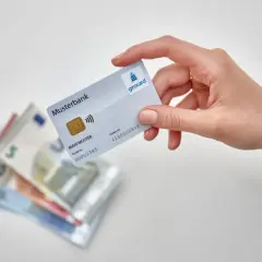 Hand hält Girocard über Euro-Scheine. So einfach ist es, mit EC-Karte im Ausland zu bezahlen und Bargeld zu sparen.