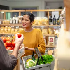 Frau kauft frisches Gemüse ein, während ein Verkäufer Tomaten anbietet. Ein Blick auf die Lebenshaltungskosten in Deutschland.