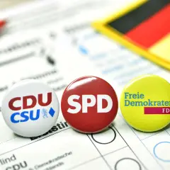 Anstecker von CDU/CSU, SPD und FDP liegen auf einem Wahlzettel. Die deutsche Flagge im Hintergrund symbolisiert die politische Landschaft für eine mögliche Deutschland Koalition.