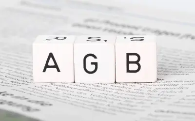 Drei Würfel mit den Buchstaben A, G, B liegen auf Zeitungstext. Ein wichtiger Schritt, um AGB zu erstellen.
