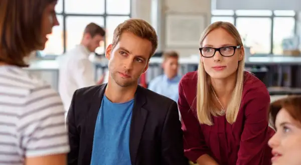 Ein Mann und eine Frau hören aufmerksam zu, während eine Kollegin spricht. Ein Beispiel für **talent mobility** in einem modernen Büro.