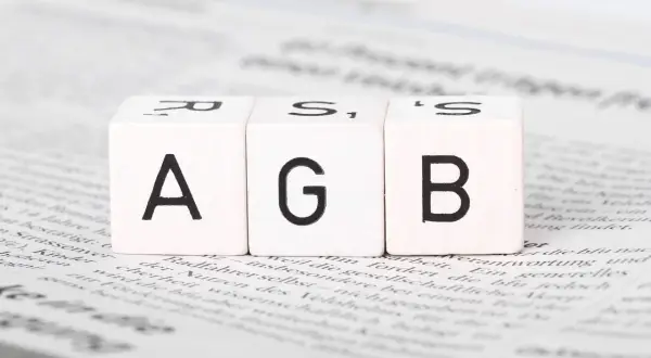 Drei Würfel mit den Buchstaben A, G, B liegen auf Zeitungstext. Ein wichtiger Schritt, um AGB zu erstellen.