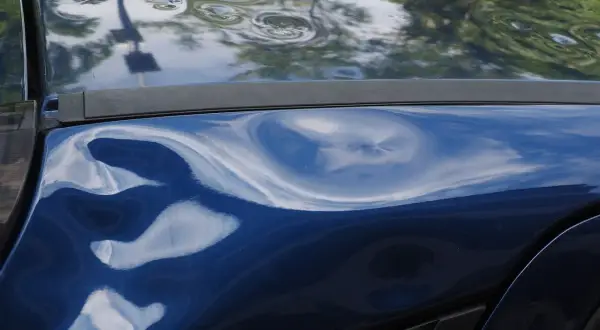 Blauer Lack mit deutlichem Hagelschaden, typisch für ein Leasingfahrzeug nach einem Unwetter.