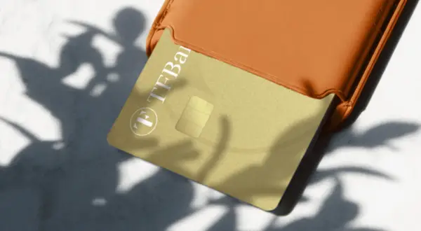 Goldene TF Bank Karte in einem orangen Etui, Schatten von Blättern. Gute TF Bank Erfahrungen sind hier zu sehen.