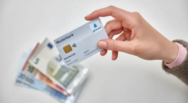 Hand hält Girocard über Euro-Scheine. So einfach ist es, mit EC-Karte im Ausland zu bezahlen und Bargeld zu sparen.