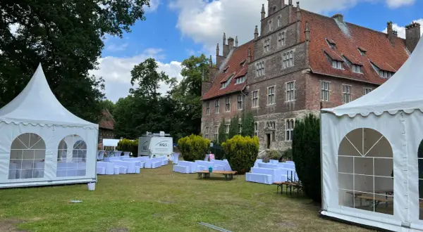 Festzelt und weiße Sitzreihen vor historischem Gebäude. Ein Anbieter für Eventausstattung hat hier alles für ein Fest vorbereitet.