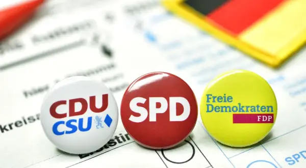 Anstecker von CDU/CSU, SPD und FDP liegen auf einem Wahlzettel. Die deutsche Flagge im Hintergrund symbolisiert die politische Landschaft für eine mögliche Deutschland Koalition.