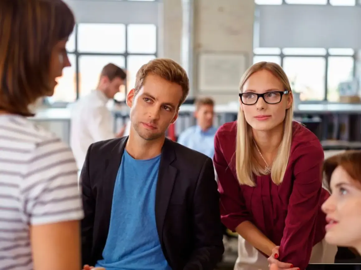 Ein Mann und eine Frau hören aufmerksam zu, während eine Kollegin spricht. Ein Beispiel für **talent mobility** in einem modernen Büro.