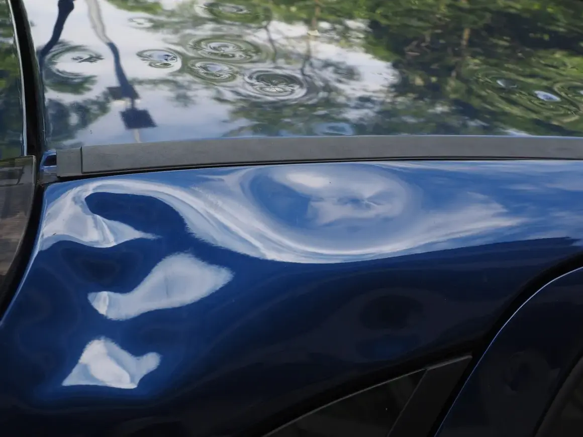 Blauer Lack mit deutlichem Hagelschaden, typisch für ein Leasingfahrzeug nach einem Unwetter.