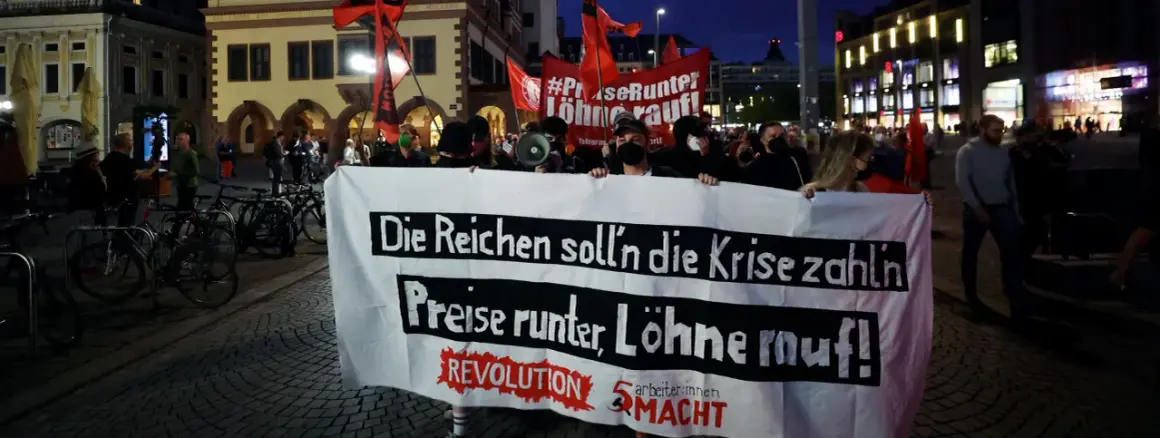 Demonstranten mit Banner "Die Reichen soll'n die Krise zahlen, Preise runter, Löhne rauf!" zeigen die politische polarisierung definition.