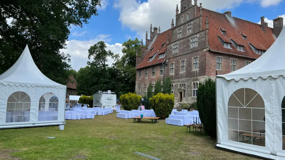 Festzelt und weiße Sitzreihen vor historischem Gebäude. Ein Anbieter für Eventausstattung hat hier alles für ein Fest vorbereitet.
