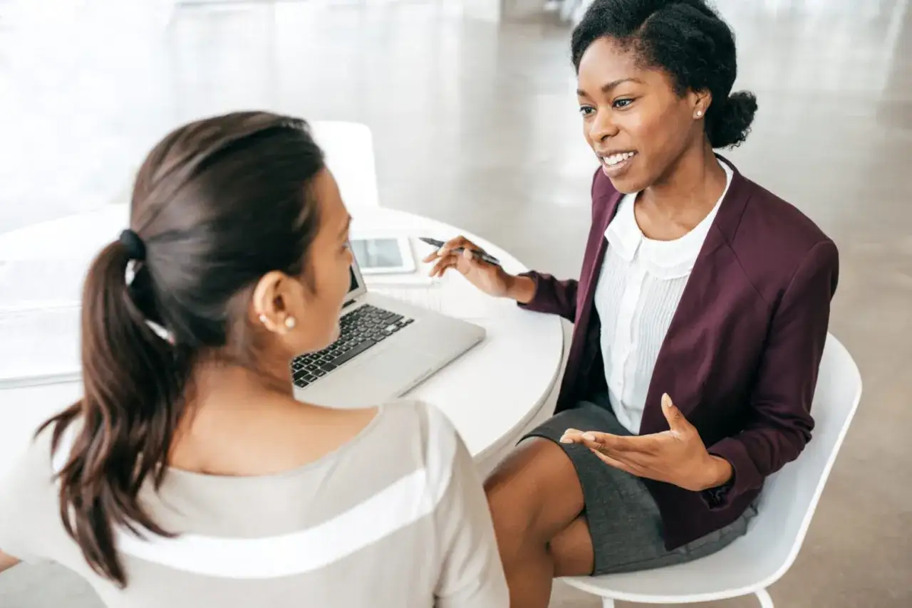 Zwei Frauen besprechen sich bei einem Meeting. Eine h&auml;lt einen Stift und erkl&auml;rt etwas, w&auml;hrend die andere zuh&ouml;rt. M&ouml;glicherweise geht es um einen exit survey.