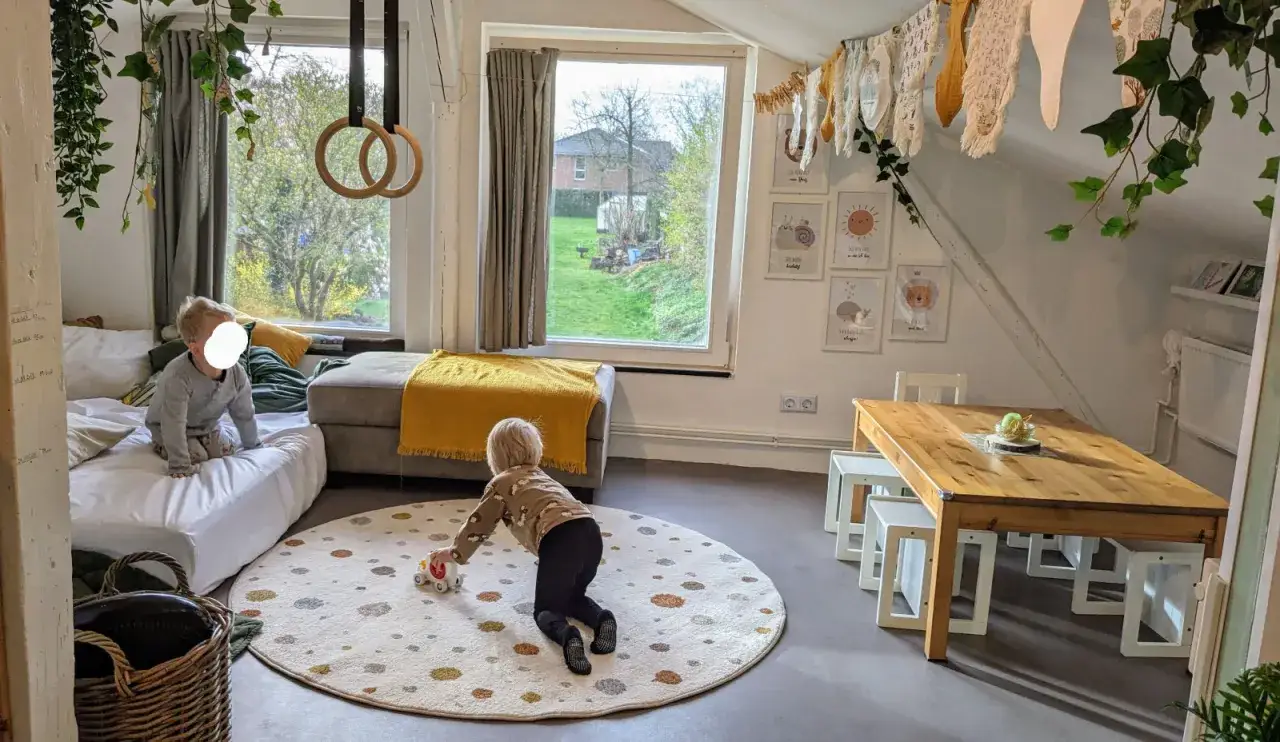 Kinder spielen in einem gem&uuml;tlichen Raum, der zum Tagesmutter werden einl&auml;dt. Ein Kind rollt mit einem Spielzeugauto, w&auml;hrend ein anderes auf einer Matratze sitzt.