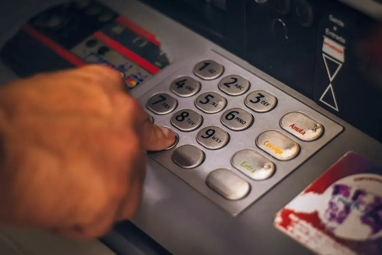 Finger drückt auf Tastatur eines Geldautomaten. Der Nutzer prüft den Kontostand, die Bedeutung des Saldos ist klar.