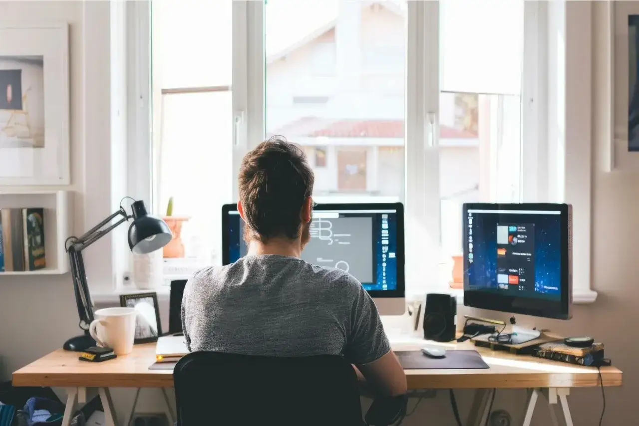 Mann arbeitet am Schreibtisch mit zwei Monitoren. Er verdient online Geld ohne Startkapital.
