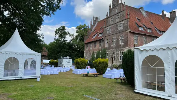 Festzelt und weiße Sitzreihen vor historischem Gebäude. Ein Anbieter für Eventausstattung hat hier alles für ein Fest vorbereitet.