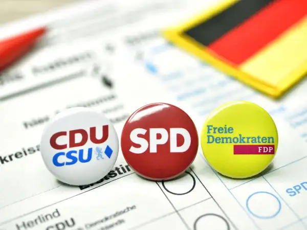 Anstecker von CDU/CSU, SPD und FDP liegen auf einem Wahlzettel. Die deutsche Flagge im Hintergrund symbolisiert die politische Landschaft für eine mögliche Deutschland Koalition.